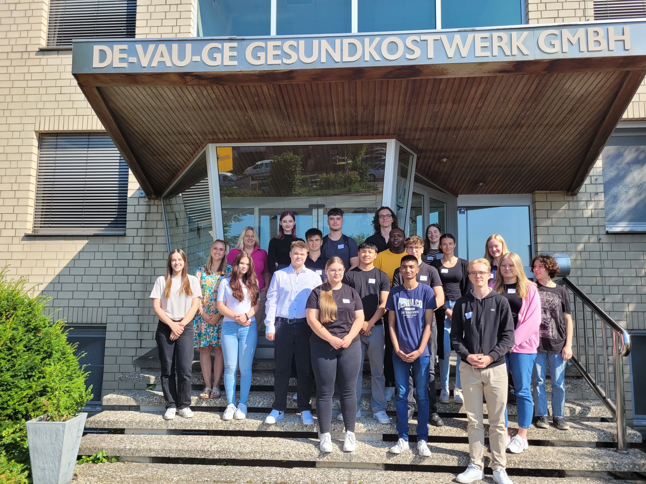 Viele Junge Menschen auf einem Bild vor einem Hauseingang auf einer Treppe.